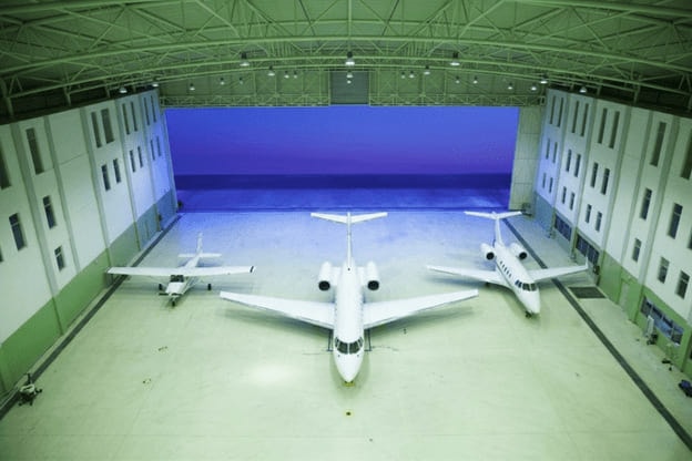 The inside of EAN’s hangar looking out through the open door at dusk, with three aircraft parked on the floor.