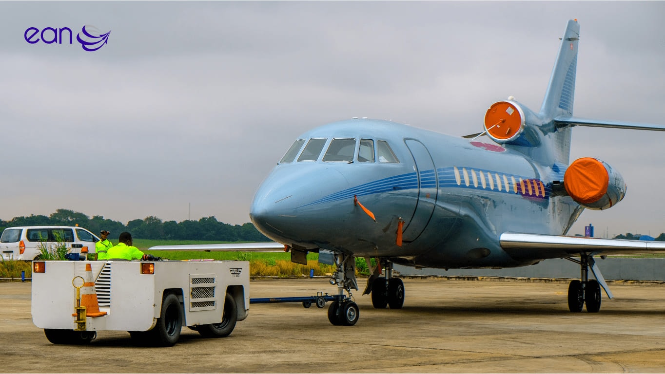 A Falcon business jet under tow on the ramp by an EAN tug, with two ground crew aboard.